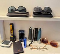 Shelf with two sunglass pairs on cases and assorted electronics below