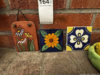 Three ceramic floral tiles on brick background