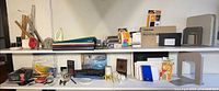 Wide view of two shelves containing rulers, folders, HP cartridges, Toshiba box, bookends and various supplies