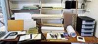 Overview of paper blocks, rolled paper, canvas, sketchbooks, tools, and storage drawers on desk and shelves