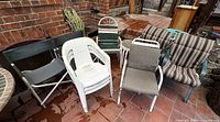 Group view of assorted patio chairs including white plastic, green plastic, green slat metal and grey sling metal chair with cushions stacked nearby