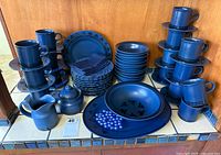 Full set stacked on counter showing plates, bowls, cups, saucers, platter, salad bowl, sugar, creamer, cloth napkins
