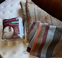 Folded comforter, striped quilt, sealed mattress pad on queen mattress
