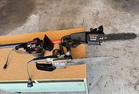 Two chainsaw heads and pole extension on table