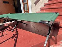 Green folding camp cot on steps, full side view