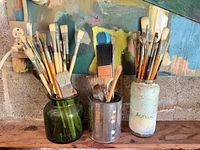Three jars holding numerous assorted paintbrushes