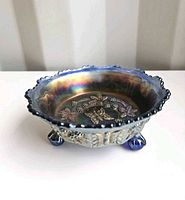 Side view of blue iridescent footed bowl showing ruffled rim and three feet