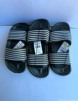 Three pairs of black slides with white stripes and tags visible