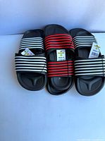 Front view of three pairs of size 3 kids slide sandals with striped uppers and tags