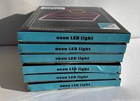 Stack of six boxed neon LED cake slice lights, box spines showing product name