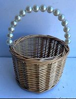 Frontal view of wicker basket showing pearl-beaded handle and weave pattern
