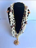 Two shell necklaces displayed on bust, pendant necklace with starburst drop, earrings on sides
