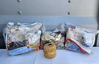 Full lot view: three clear bags with mixed crafting contents and ball of tan cord