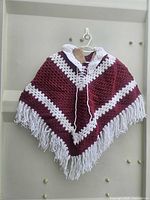Full view of shawl hanging, showing maroon body, white chevron stripes, fringe