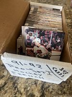 Cardboard box containing neatly organized stack of Pro Set 1991-92 Series 1 hockey cards, sample card visible showing NHL player
