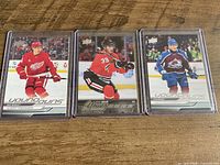 Three Upper Deck Young Guns hockey rookie cards in top loaders displayed on wooden surface