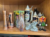 Full lot on shelf showing steins, copper vases, tin, art glass, frogs, clown
