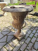 Front view of one beige concrete urn showing laurel relief and pedestal base