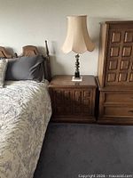 Nightstand beside bed showing paneled doors and lamp on top