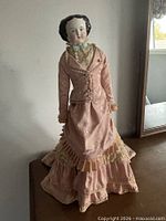 Front view of china doll wearing pink Victorian dress on stand