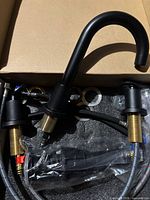 Faucet components in box showing spout, mounting stems, hoses, hardware