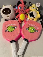 two pink fuzzy pickleball paddles and three plush toys