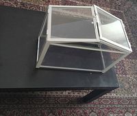 Three-quarter top view showing white frame, clear panels, one roof section open, placed on black table