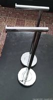 Two chrome toilet roll holders standing upright showing full view