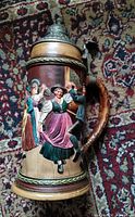 Front view of ceramic beer stein with relief dancers and pewter lid