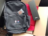 Backpack atop red blanket with maple leaf pin and SRG water bottle box in shipping carton