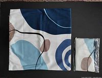Blue-white abstract pillow case laid flat next to packaged matching case