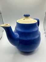 Front angled view showing blue ceramic body, cream lid, handle and spout