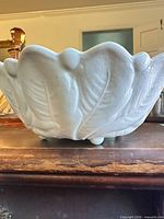 Side view of white cabbage-leaf ceramic bowl showing leaf relief and footed base