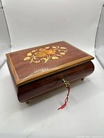 Closed wooden jewelry music box front angle showing overall form, brass feet visible