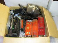 Open box showing transformer on top, multiple red passenger cars and black parts