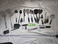 Full view of 20 assorted utensils laid out with tape measure for scale