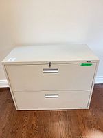 Front view of beige 2-drawer metal lateral file cabinet showing lock and pulls