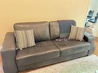 Front view of black leather sofa with two throw pillows and blanket