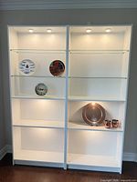 Front view of both illuminated bookcases showing glass shelves and decorative items
