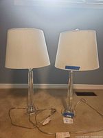 Front view of both clear acrylic lamps with white shades and cords visible