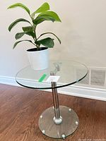 Side view of round glass top table with chrome stem and faux plant in pot