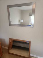 Both mirrors shown; silver wall mirror mounted, oak wood mirror leaning below.