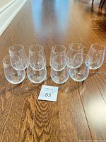 Nine clear stemless wine glasses displayed on hardwood floor