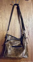 Front view of brown handbag hanging, showing adjustable strap and exterior zip pocket
