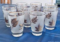 Front angled view of all eight frosted tumblers showing gold leaf motif and gold rims