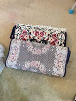 Two rolled floral oriental area rugs showing fringe and backing