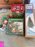 Lot overview showing boxed tree, musical bell lights, bag with multi-color lights, lampshades, plush figures, clips