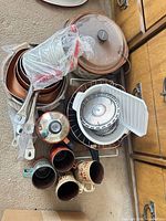 lot overview showing stacked pans, saucepan, slow cooker insert with lid, steamer basket in plastic container, seven mugs