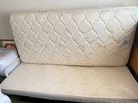 Twin mattress leaning against wall showing quilted floral cover and base below