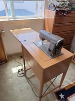 Kenmore sewing machine mounted in wood cabinet with extension leaf deployed; stack of fabric visible on adjacent surface